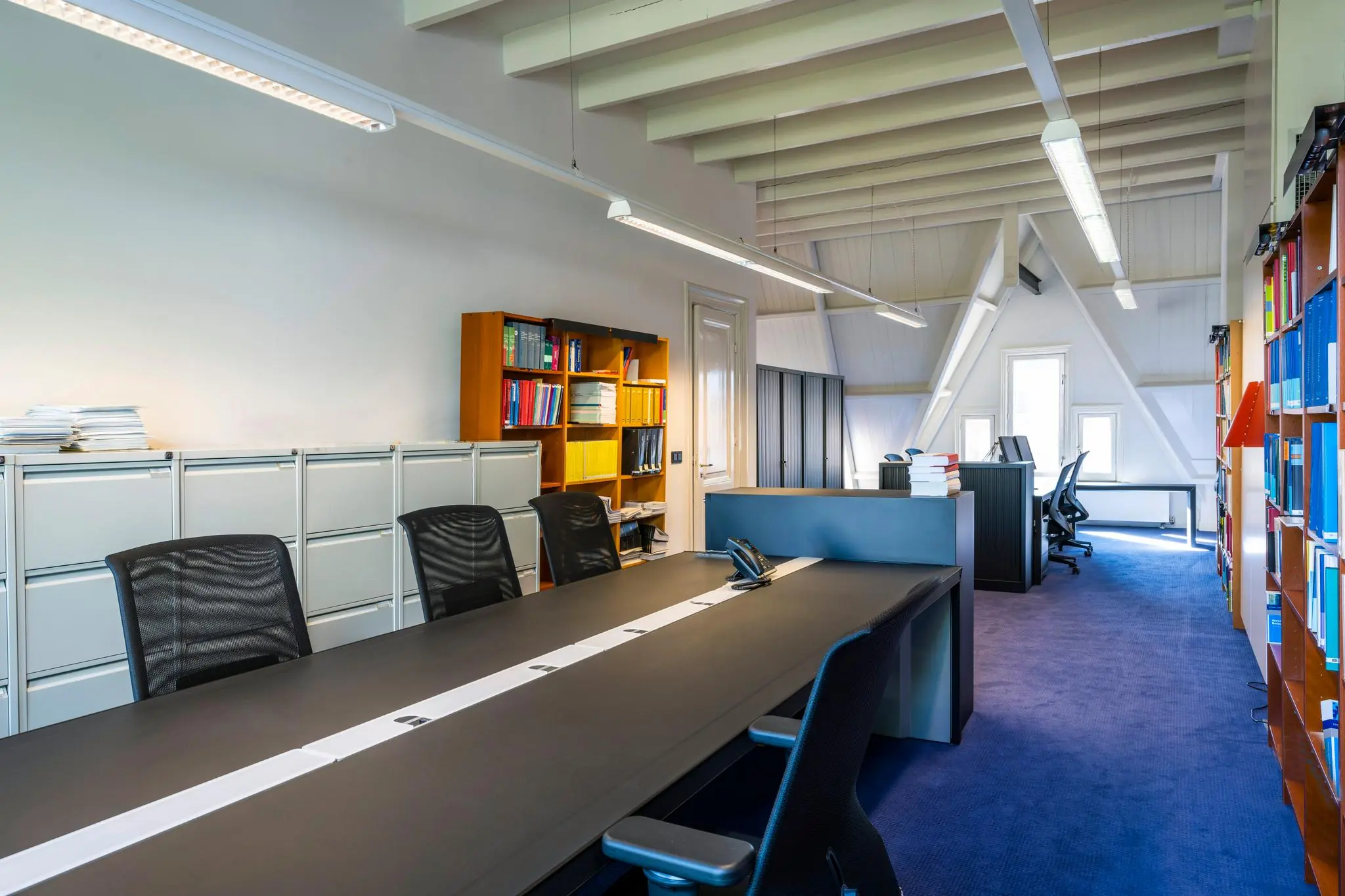 Modern kantoorinterieur aan de Paulus Potterstraat met bureaus, archiefkasten en boekenkasten onder een schuin plafond.